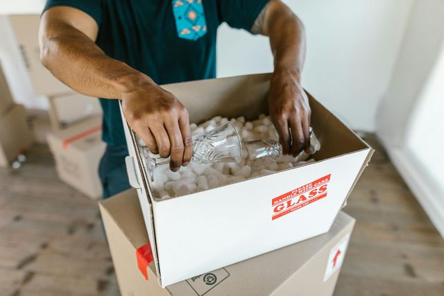 Person packing glasses in a cardboard box with 