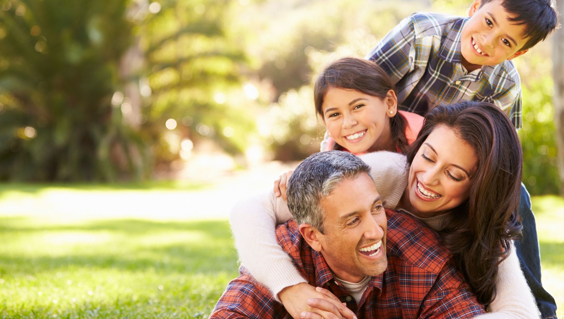 a family is sitting on top of each other in the grass in a park .
