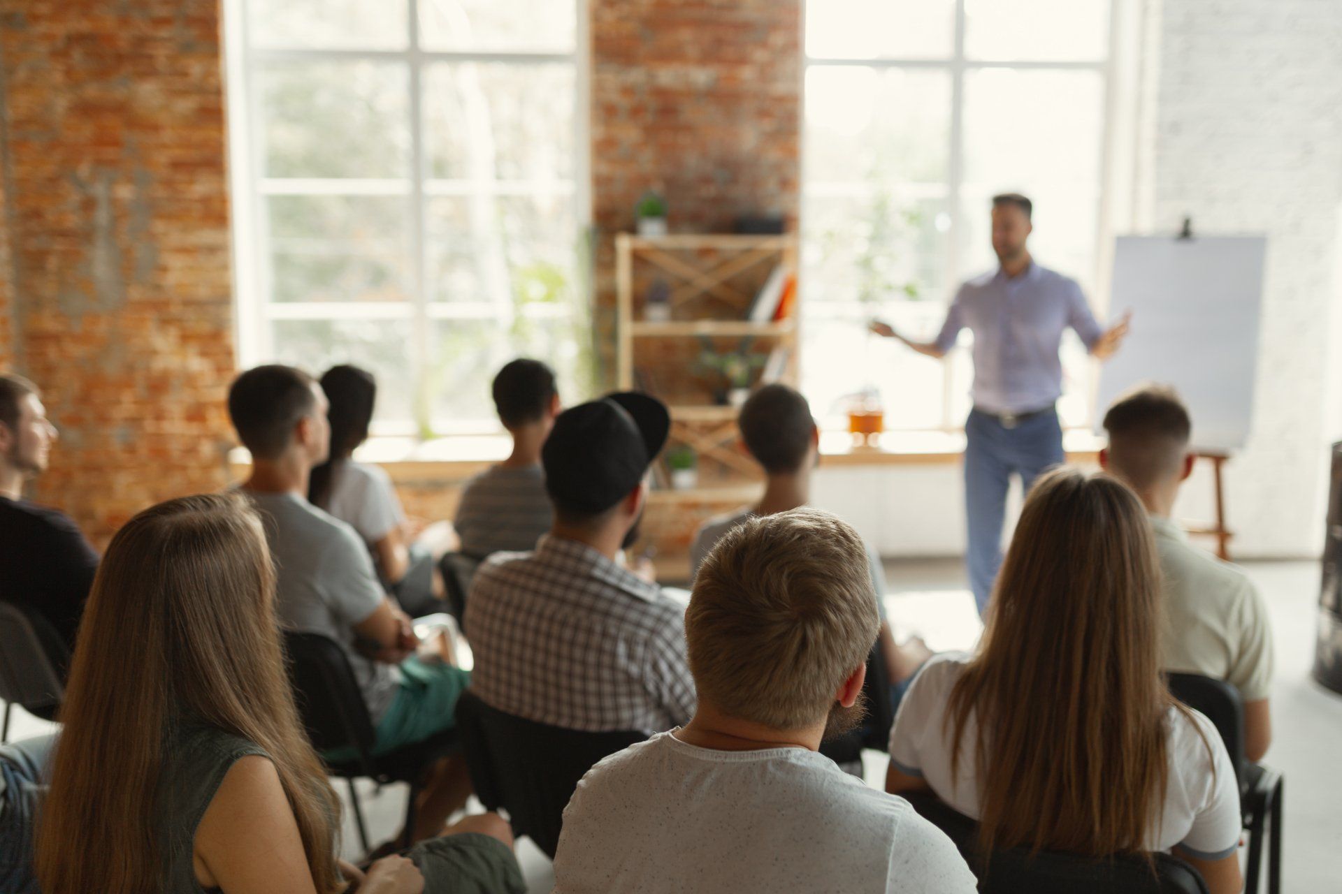 Male speaker giving presentation in hall at university workshop. Audience or conference hall. Rear view of unrecognized participants in audience. Scientific conference event, training. Education