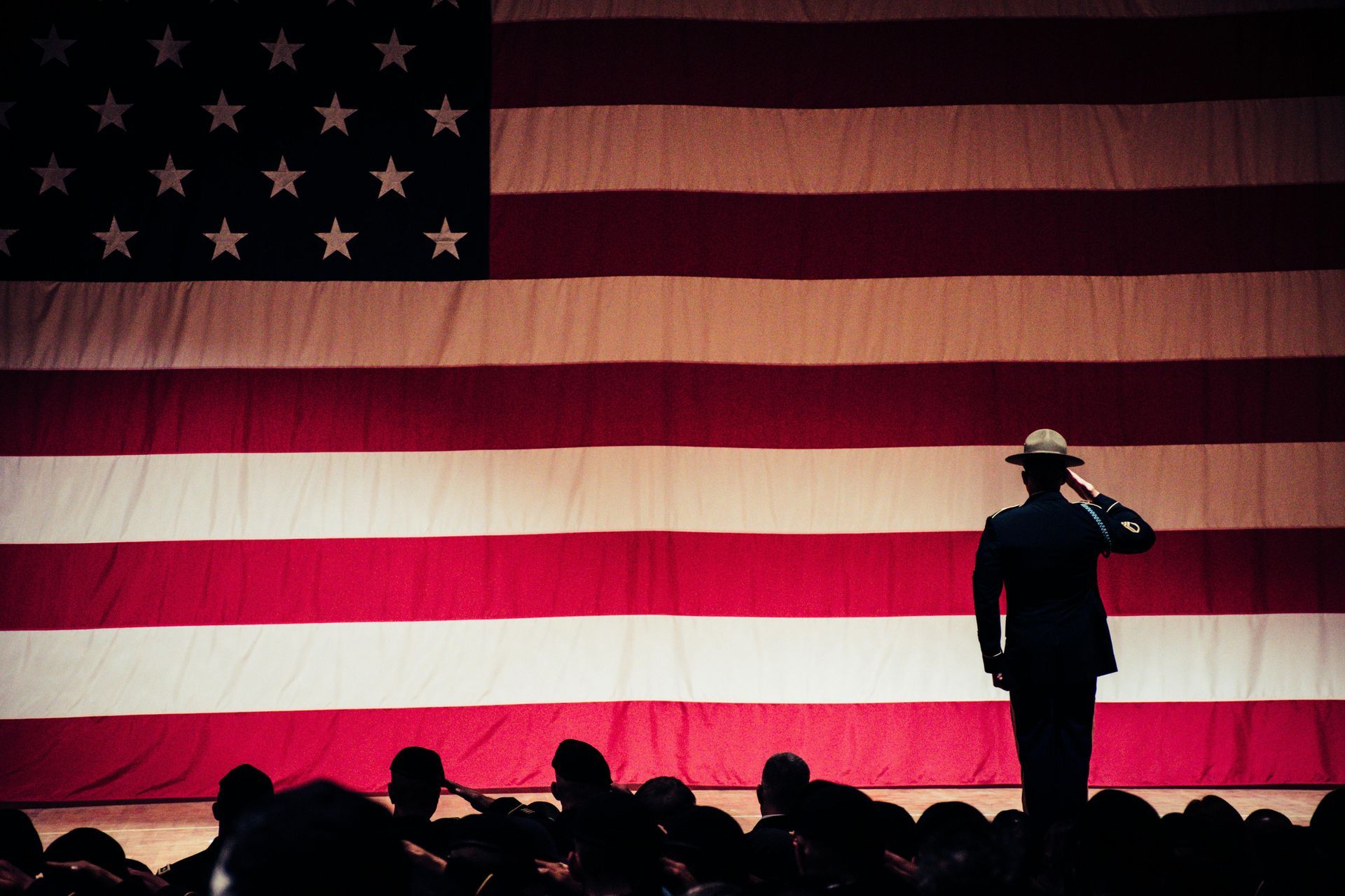 Soldier salutes large American flag; others salute in the foreground.