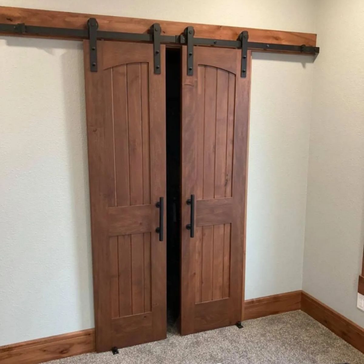 Double solid wood sliding barn doors mounted on black metal track hardware, creating a space-saving