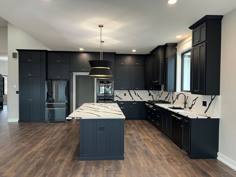 A kitchen with black cabinets and a large island in the middle.