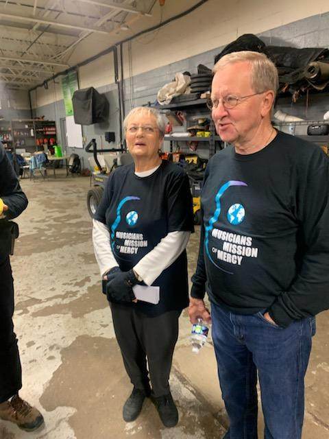 A man and a woman are standing in a garage wearing t-shirts that say worldwide mission ready