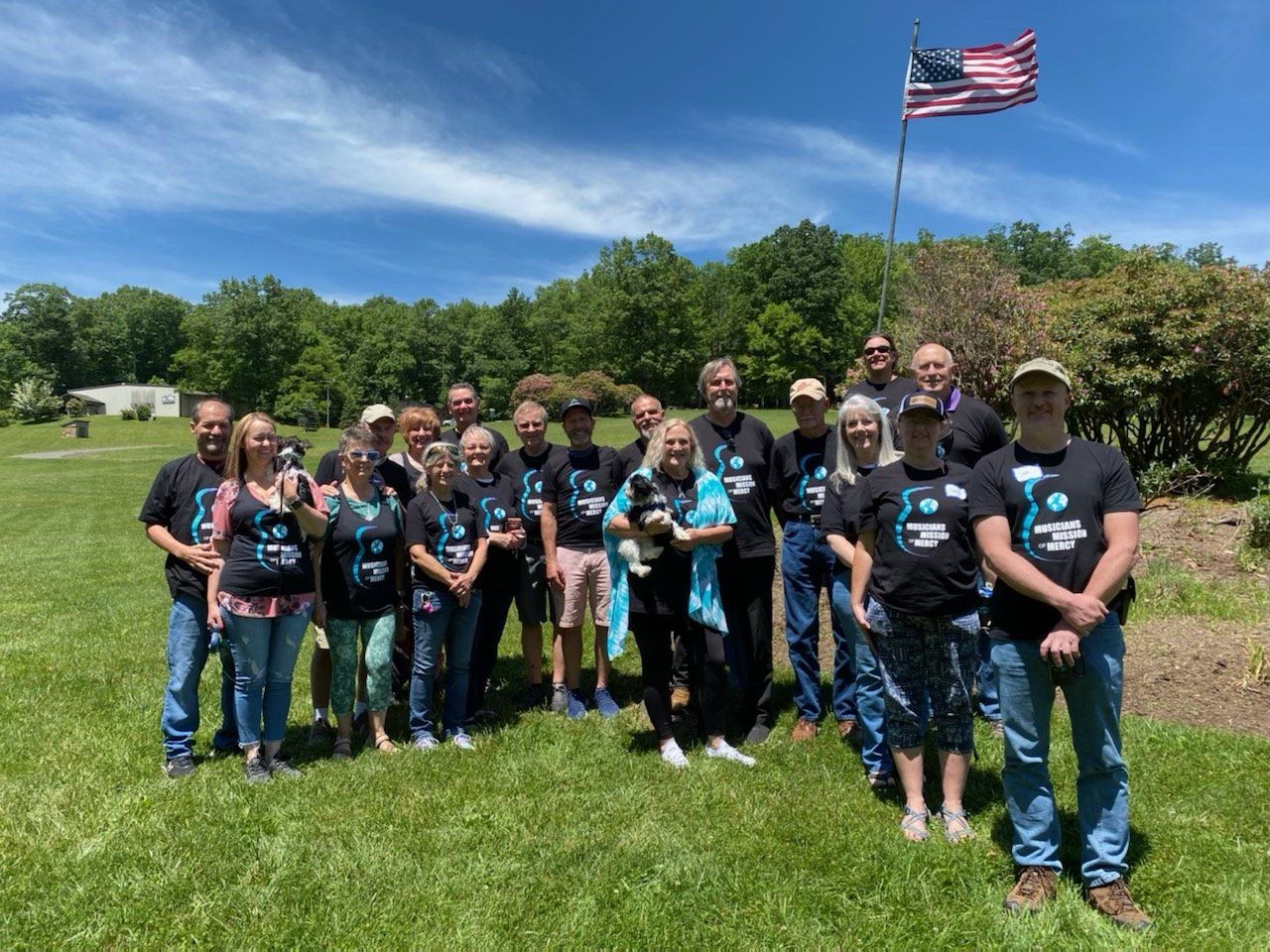 A group of people are standing in a field with an american flag in the background.