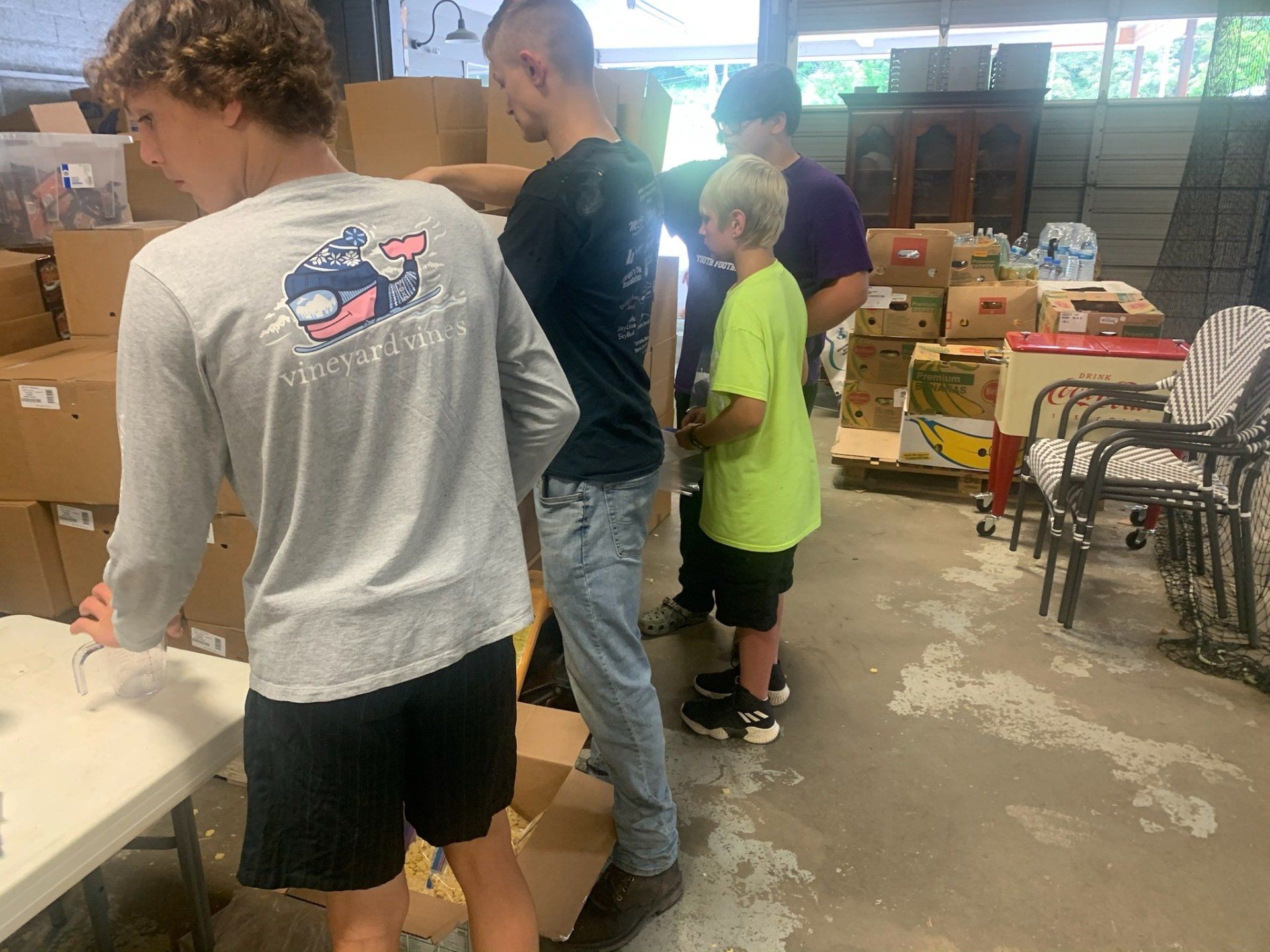 A group of people are standing in a room filled with boxes.