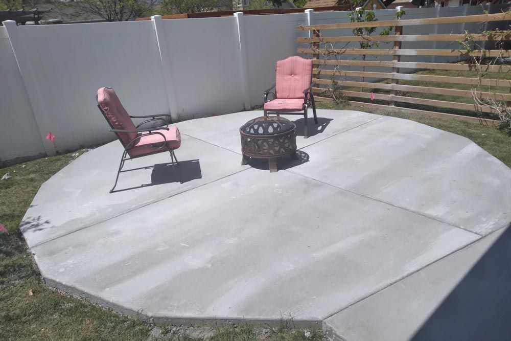 Backyard patio with two pink chairs and a fire pit on a large concrete pad