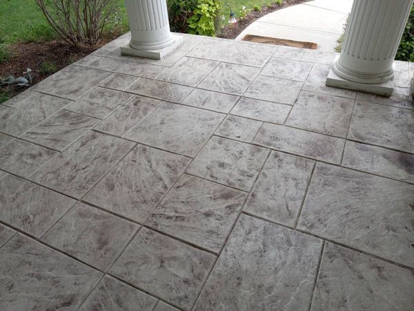 Stone-tiled front porch with two white columns and a curved walkway to the right