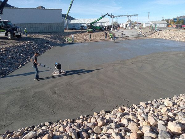 Two workers smoothing wet concrete at a construction site beside rocks and buildings