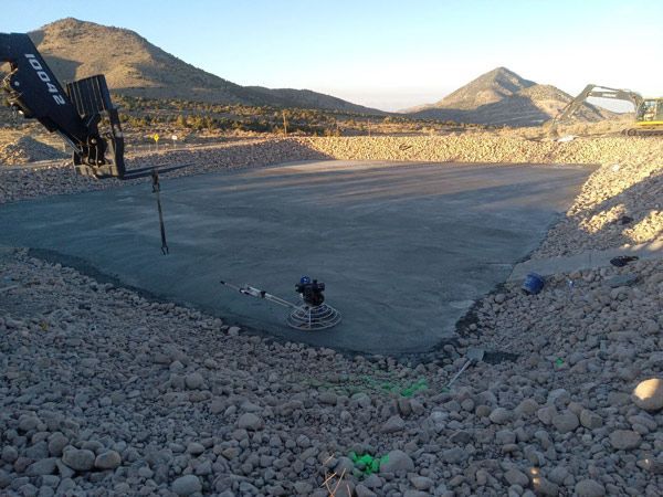 Concrete foundation slab at a construction site, surrounded by rocks with mountains in the background.