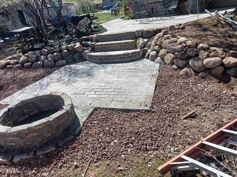 Stone steps and retaining walls in a landscaped yard with a circular fire pit and gravel ground.