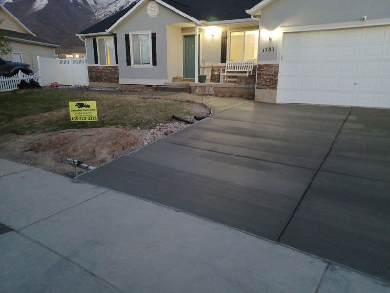 Suburban house with lit porch, concrete driveway, and a small lawn sign at dusk