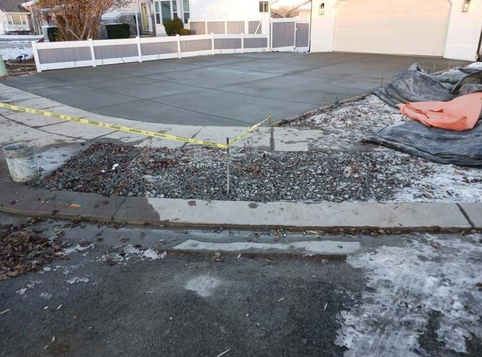 Damaged driveway with broken curb and debris, next to a newly poured concrete slab