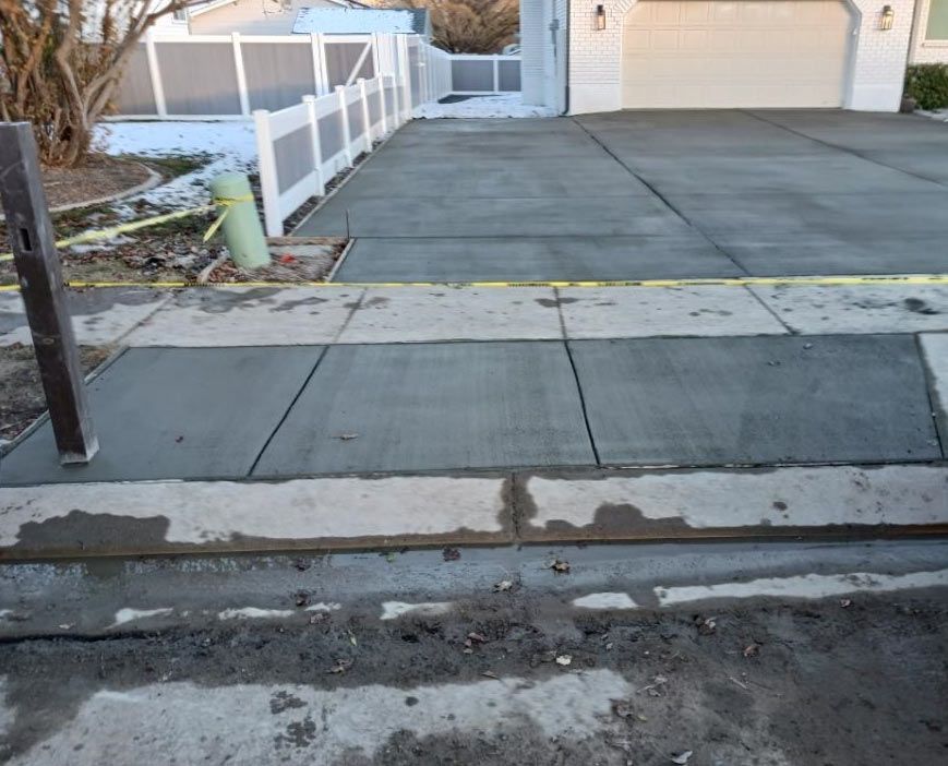 Cracked sidewalk curb ramp leading to a driveway and garage with a white fence and yellow tape.