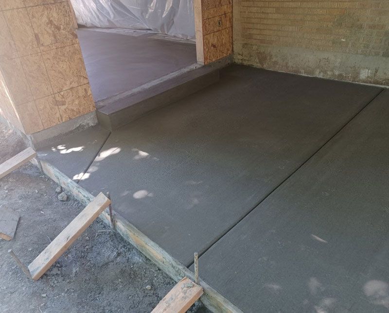 Freshly poured concrete floor inside an unfinished room with brick walls and wooden forms.