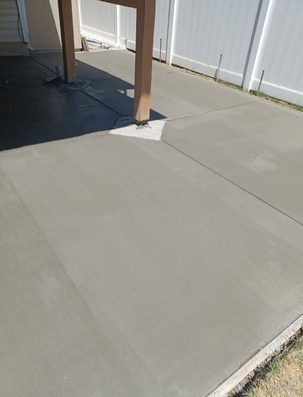 Concrete patio beside a white fence and house post in bright sunlight