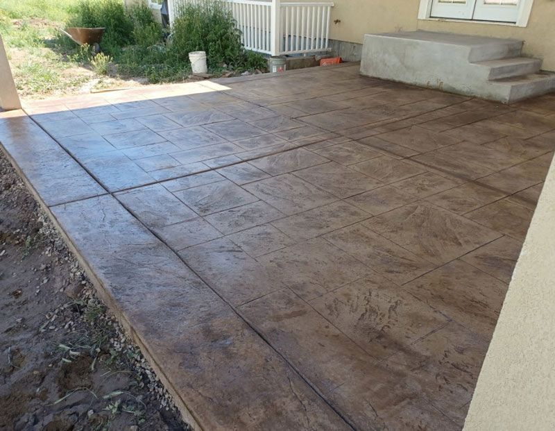 Covered concrete patio with stamped surface and steps beside a house porch