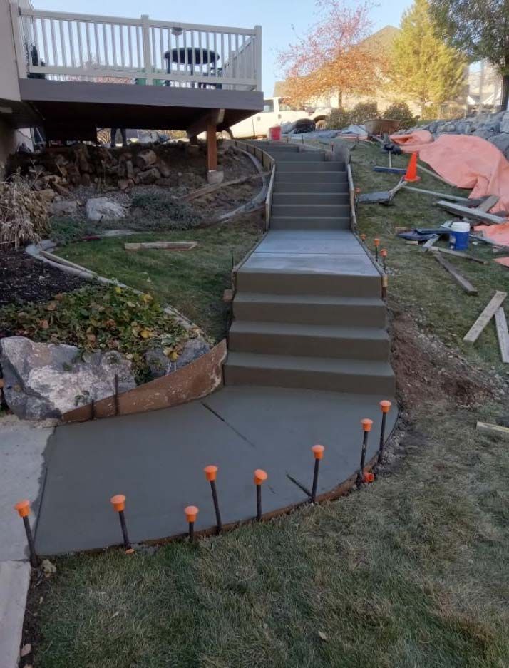 Backyard staircase and curved concrete path leading to a deck, with orange path lights and retaining walls