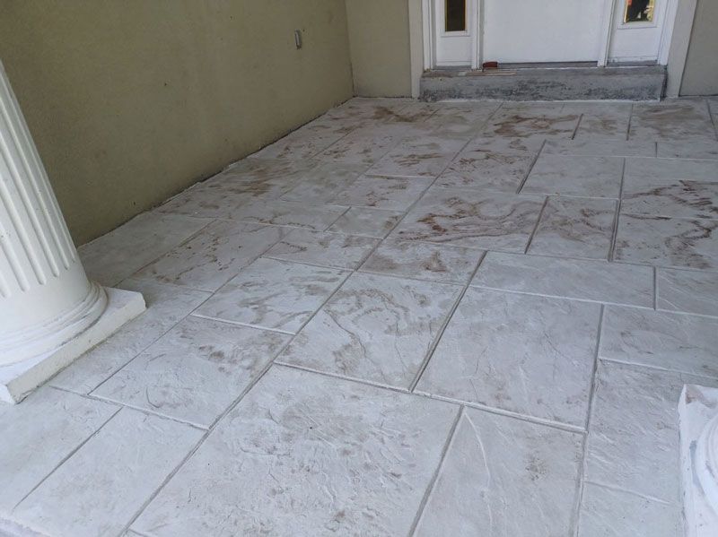 Stone-tiled front porch with white column and double doors, showing visible dirt or stains on the floor