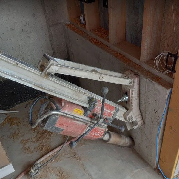 Broken red hydraulic door closer on a stairwell floor, with exposed wood railing and dusty concrete nearby