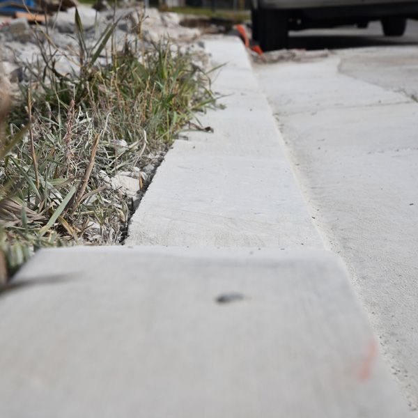 Low-angle view of a concrete sidewalk beside dry grass and a parked vehicle in the background