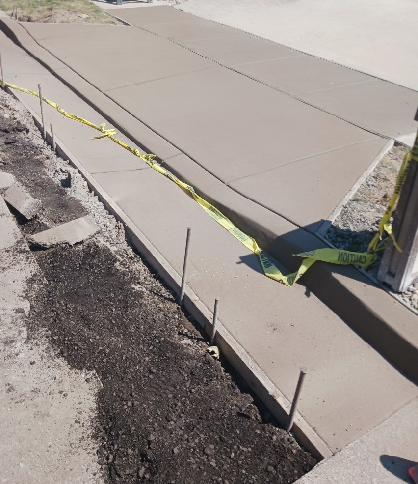 Broken sidewalk with caution tape cordoning off a damaged concrete section near a street curb