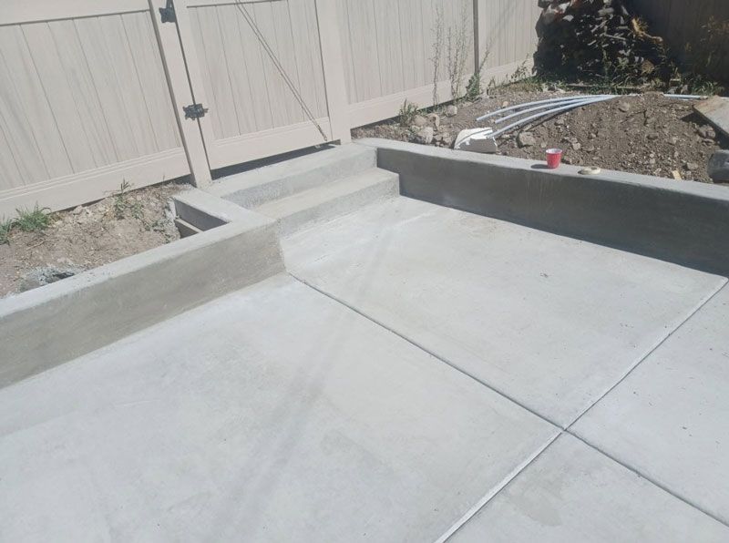 Concrete patio with low retaining walls and a wooden fence in the background