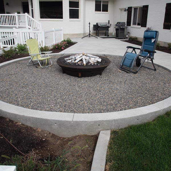 Patio with fire pit, folding chairs, and grill on a gravel-covered backyard seating area