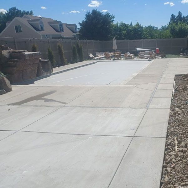 Empty concrete patio with stone seating and a fence beside a house under a blue sky