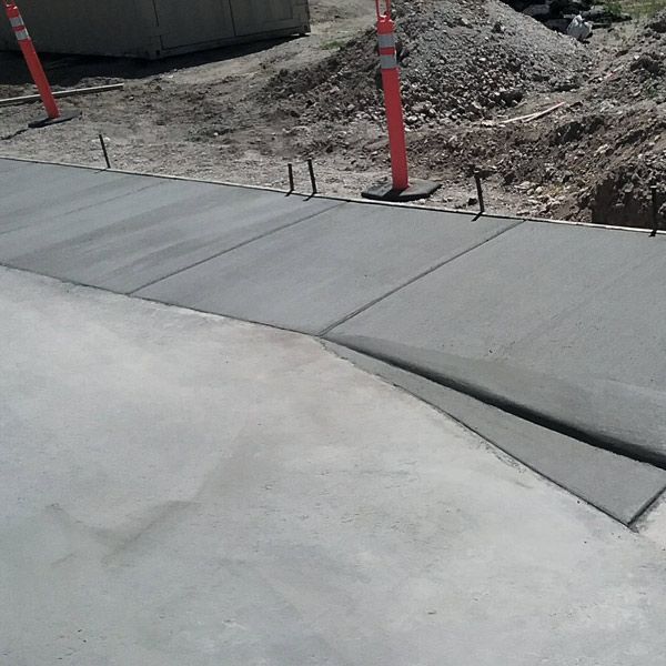 Concrete sidewalk ramp beside a dirt construction area with orange safety posts and a curb cut.