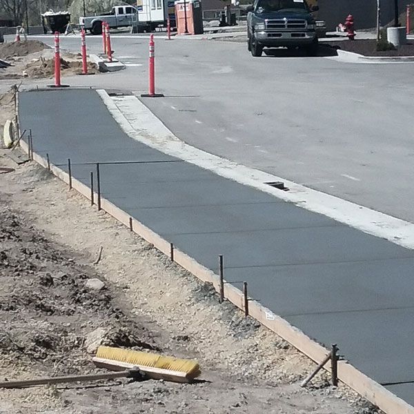Fresh concrete sidewalk along a street construction area with orange cones and a pickup truck in the background