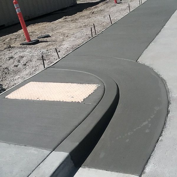 Curb ramp with tactile paving beside a new concrete sidewalk on a street corner