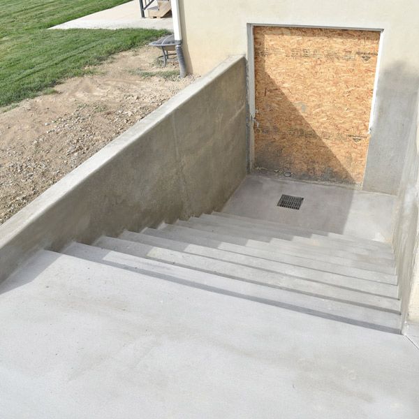 Concrete stairwell descending to a boarded-up basement entrance beside a building.