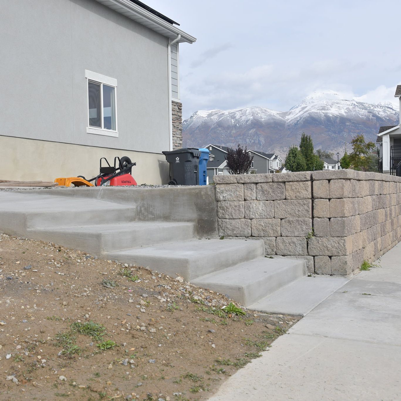 Concrete steps beside a house, with a stone retaining wall and snowy mountains in the background.