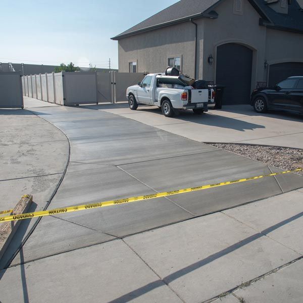 Concrete driveway beside a garage with a white pickup truck and yellow caution tape in the foreground