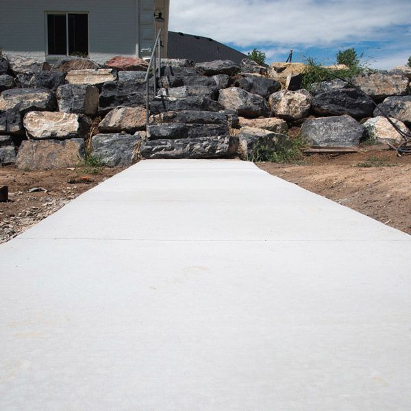 White concrete walkway leading to a stone retaining wall under a partly cloudy sky
