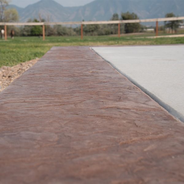 Low stone curb beside a concrete path, with grass, a fence, and mountains in the background