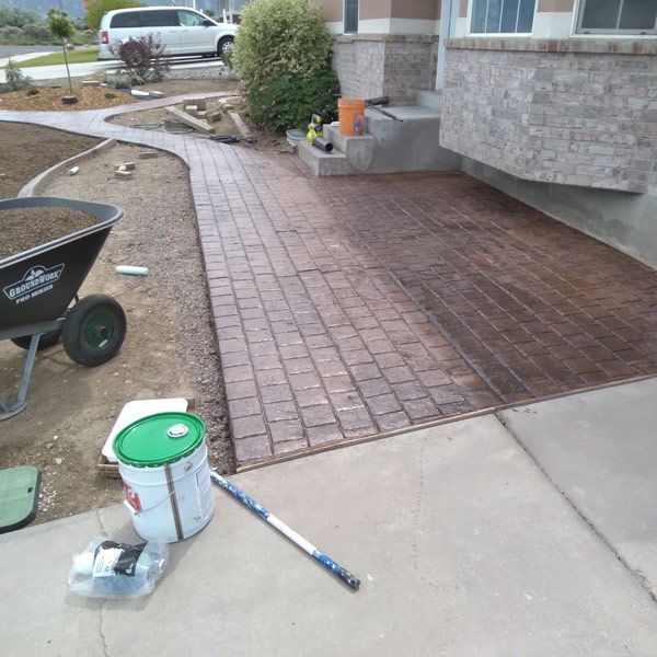 Freshly laid red brick paver patio beside a house, with tools and paint bucket on the ground.