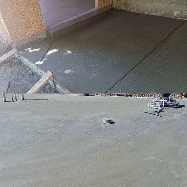 Freshly poured gray concrete floor in an indoor construction area with a trowel and tools nearby
