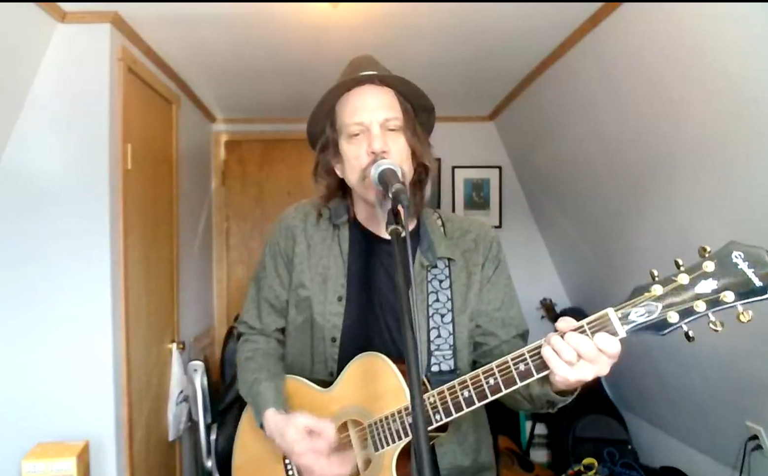 Man singing into a microphone while playing acoustic guitar in a small room