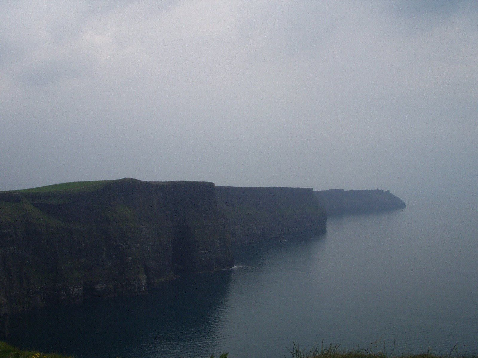 Cliffside coastline fading into a misty gray sea under an overcast sky