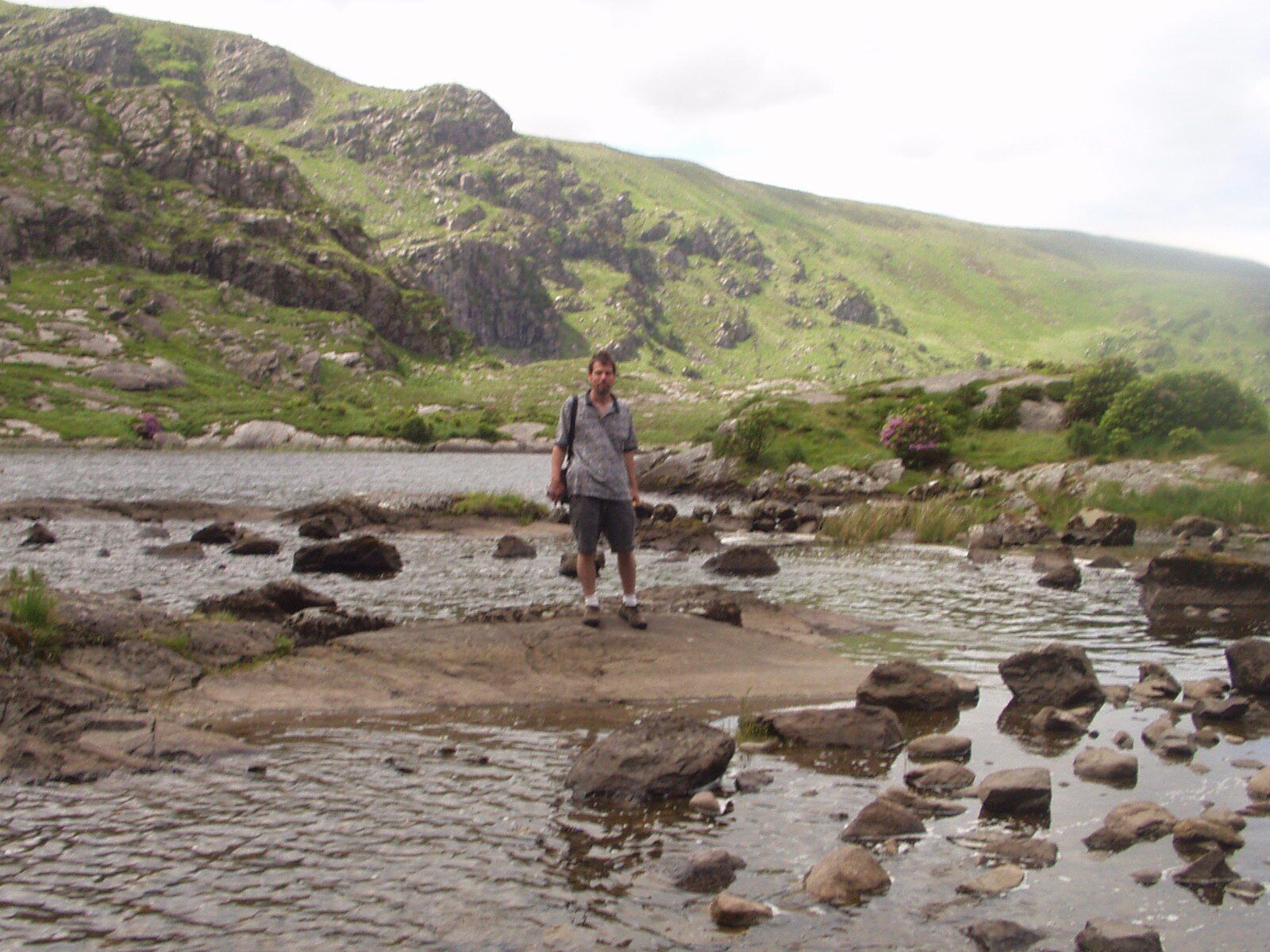 Person standing on rocks in a shallow river with green hills in the background