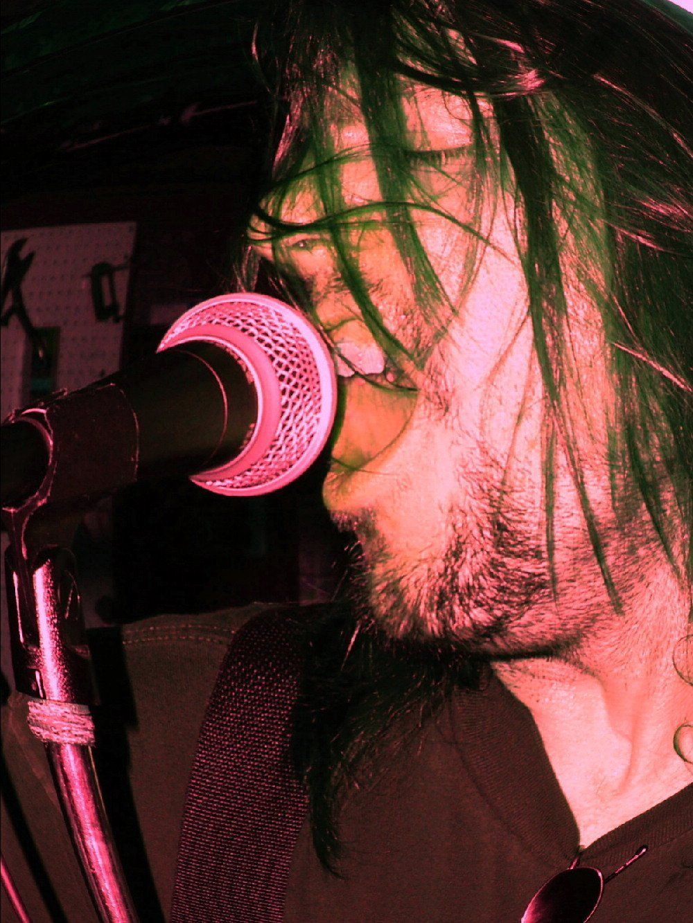 Singer performing into a microphone under pink stage lighting, side profile close-up