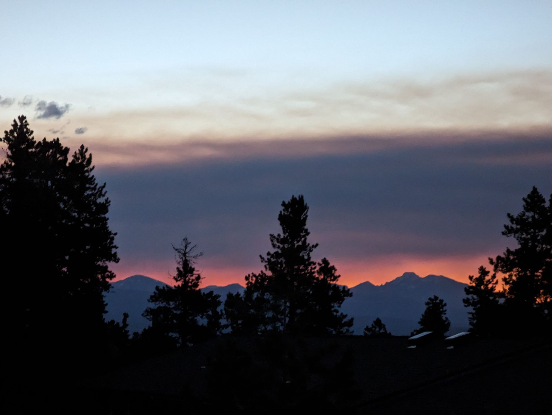 Silhouetted trees against a purple-pink sunset over distant mountains and a calm horizon