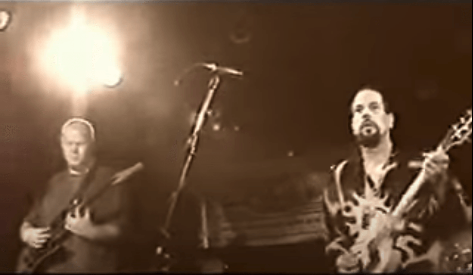 Two musicians onstage under warm lights, one singing into a microphone while playing guitar.