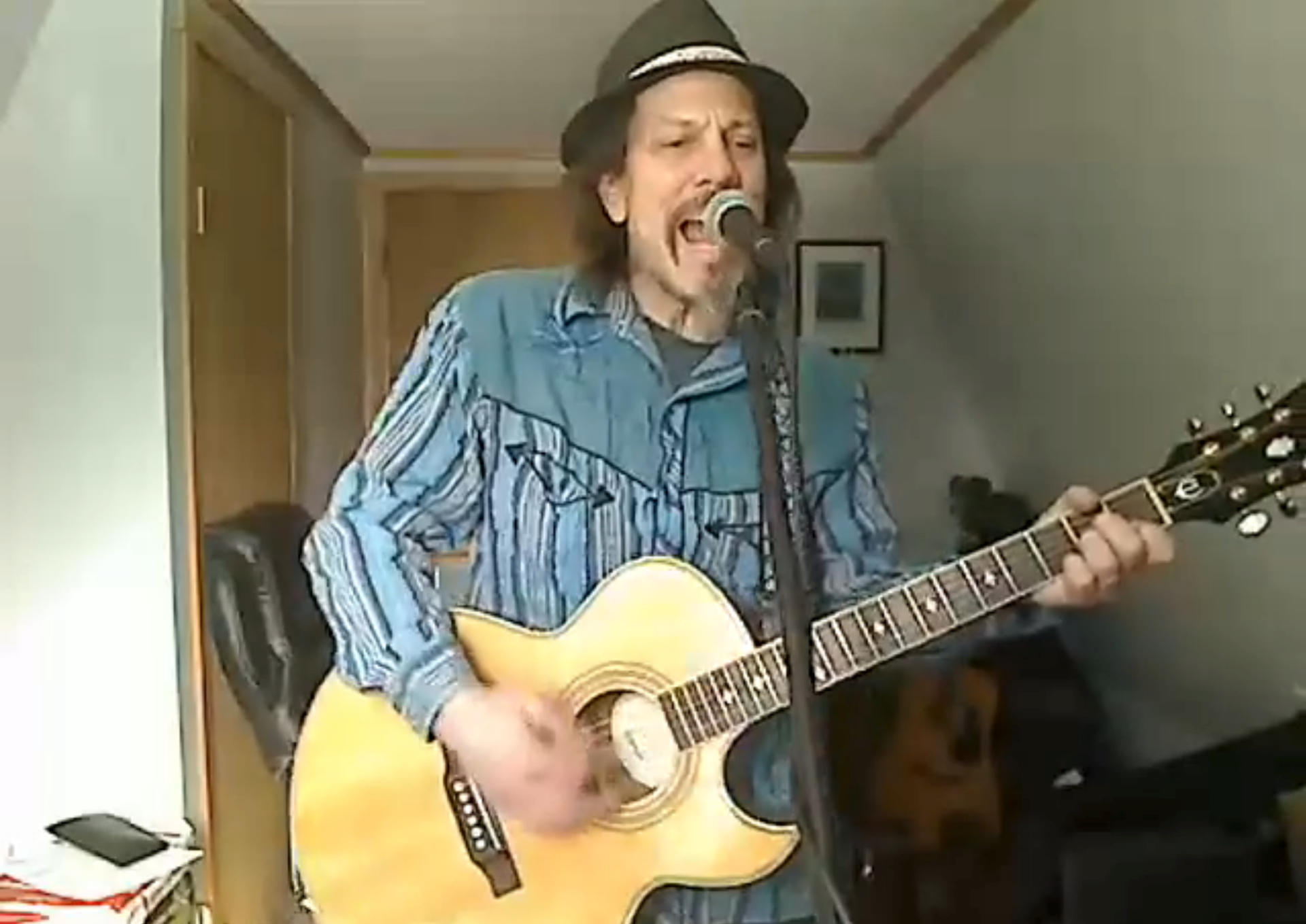 Person singing and playing acoustic guitar into a microphone in a small room