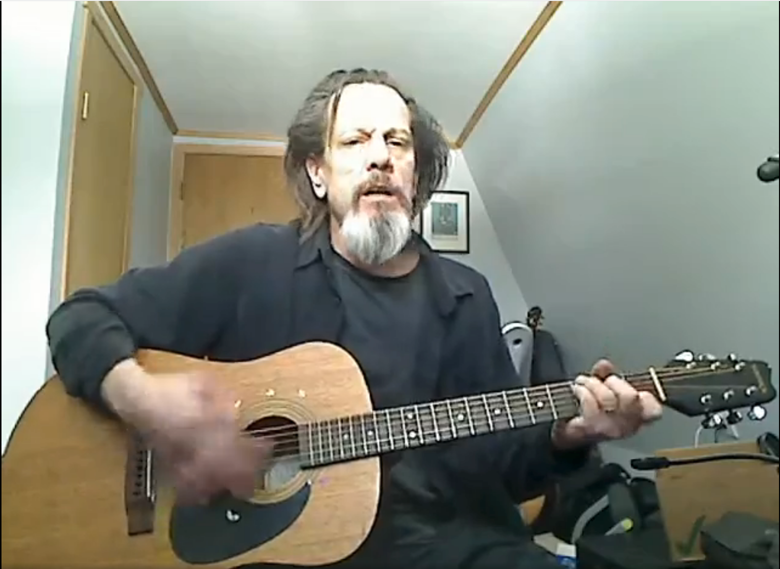 Man seated indoors playing an acoustic guitar in a small room