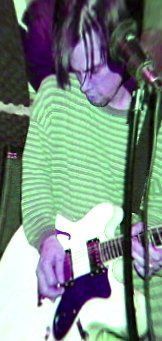 Person in a green striped sweater playing a white electric guitar on stage