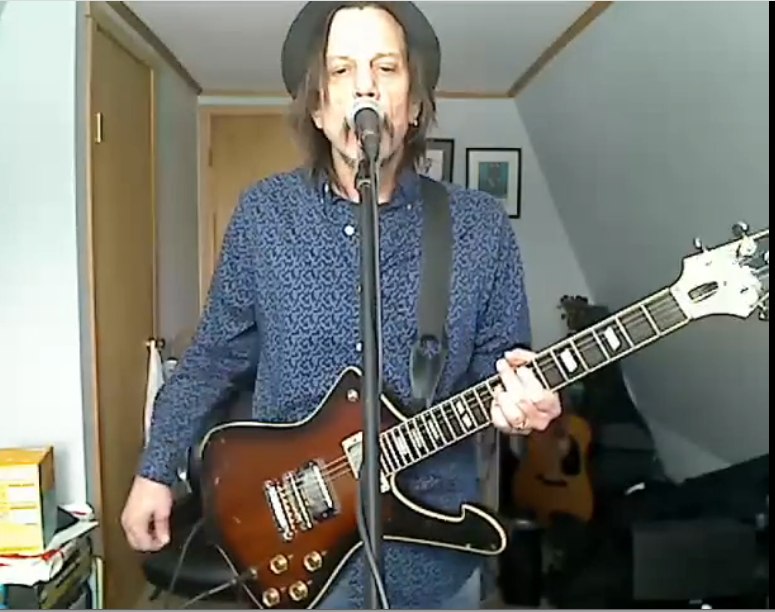 Musician singing into a microphone while playing an electric guitar in a home room
