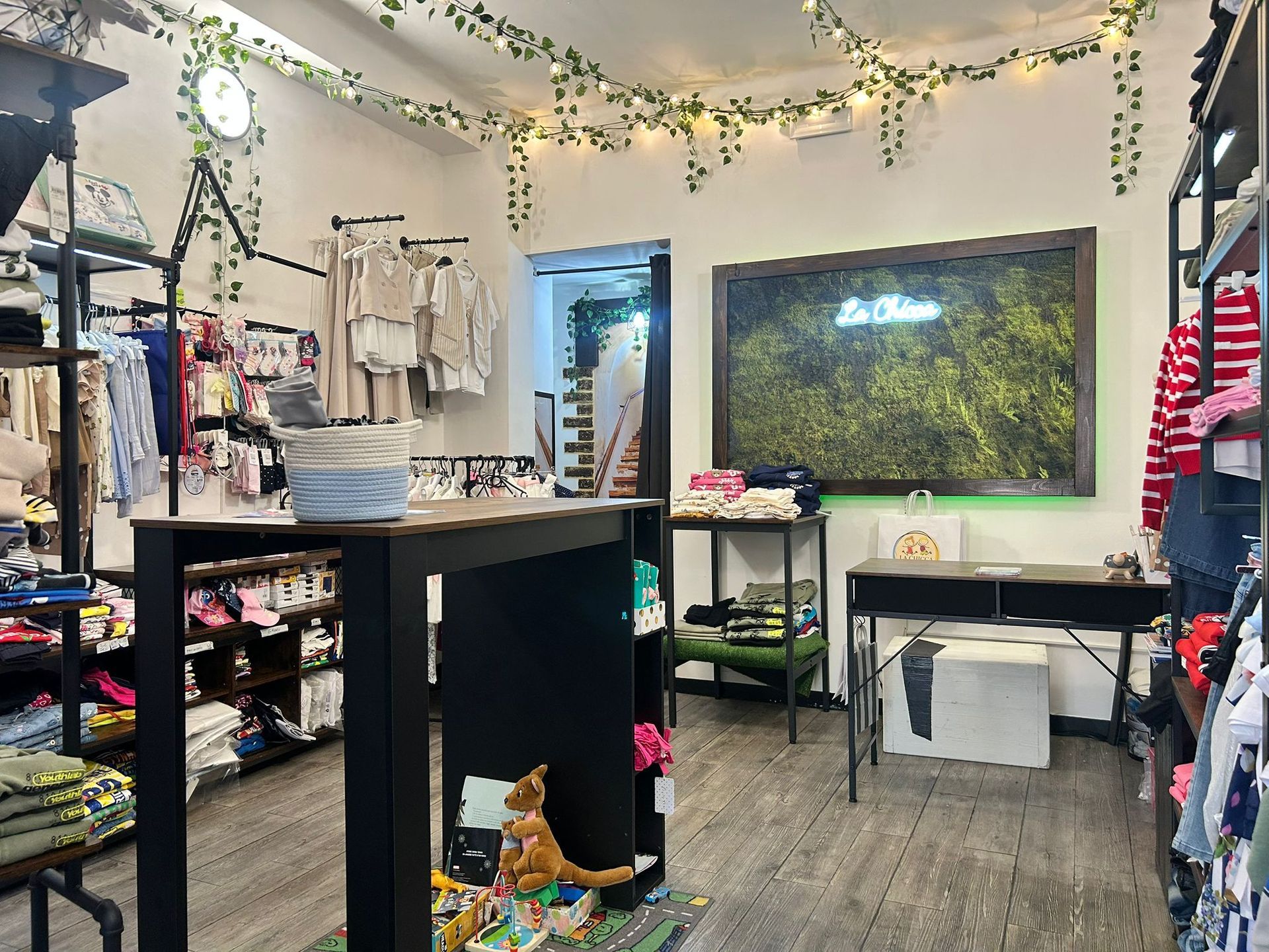 Interno di una boutique con appendiabiti, bancone e una grande opera d'arte raffigurante una foresta verde sulla parete.