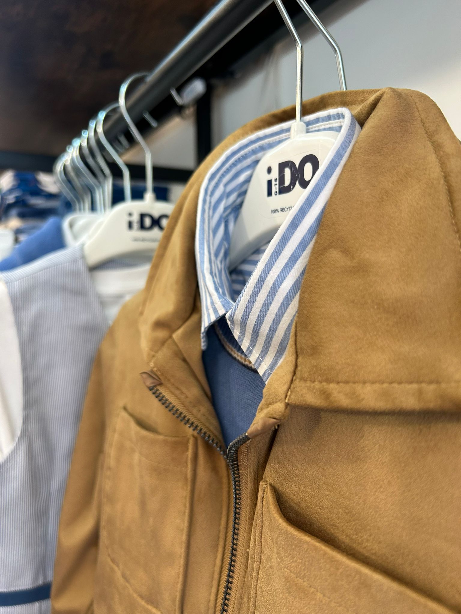 Giacca color cammello appesa a uno stendino, con il colletto della camicia a righe ben visibile.